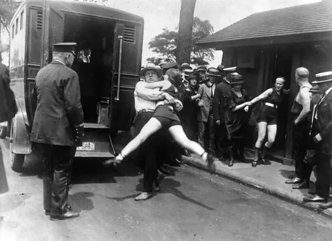 Women getting arrested due to improper bathing suit measurements, 1920s.