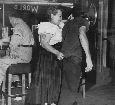 Cairo Mary, bouncer at Shanghai Red's in San Pedro, California, escorts a customer to the door  in 1953.