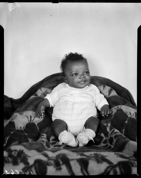 Happy chubby baby gifting smiles from his little throne, circa 1940s.