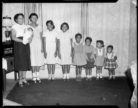 Mother smiles with her 8 children, all from oldest to youngest with the new one on her arms, circa 1950s. Safety film.