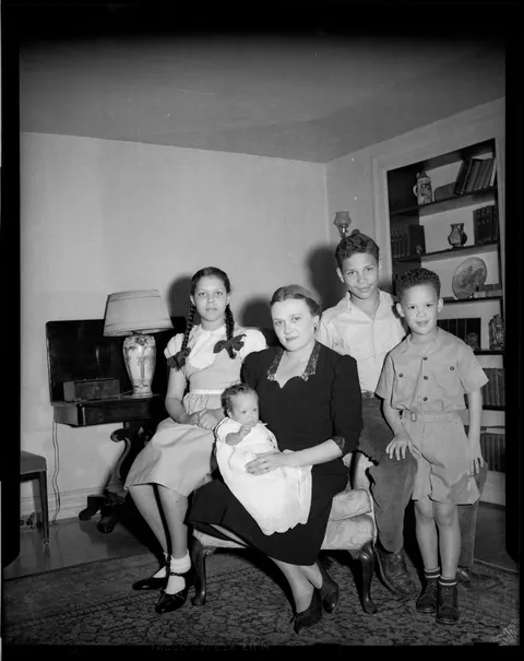 Blonde lady posing with her baby and her three older children on her living room. circa 1950s.