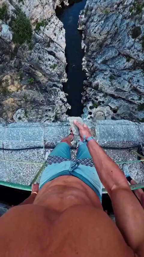 First-person perspective of professional cliff jumper Jeremy Nicollin leaping from a 31-meter-high bridge over a canyon into a small river.