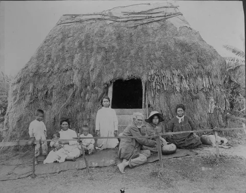 Hawaiian family in front of thatched grass house, 1890-1930