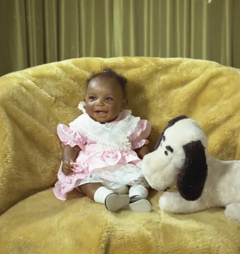 Little baby girl gives a nice smile while posing with her snoopy plush, 1975.