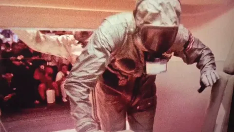 What is the ball dangling from the right side of the Apollo 11 crews' respirator hoods when entering the MQF on the USS Hornet?