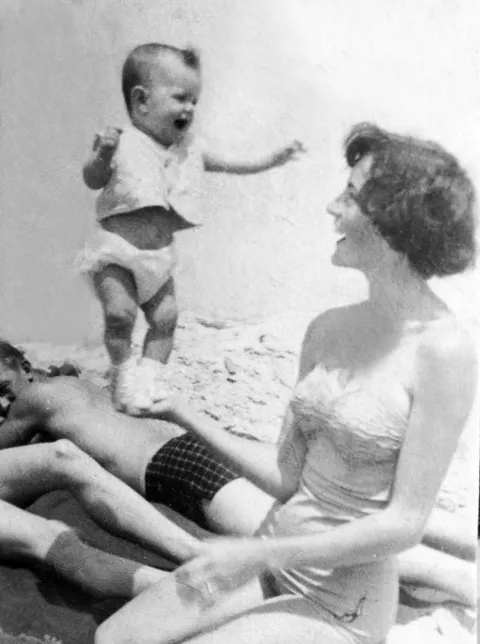 Woman has fun doing a balancing act with her baby in the palm of her hand while on the beach. The baby seem to be having the time of her life, circa 1940s.