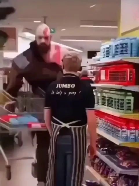 A man, strikingly resembling the God of War, roams through the market—an imposing presence that turns every head.