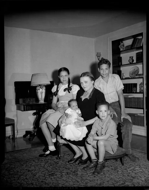 Blonde lady posing with her baby and her three older children on her living room. circa 1950s.