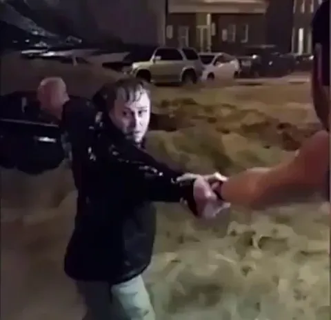Bystanders form a human chain in a flash flood to pull a driver from a sinking car