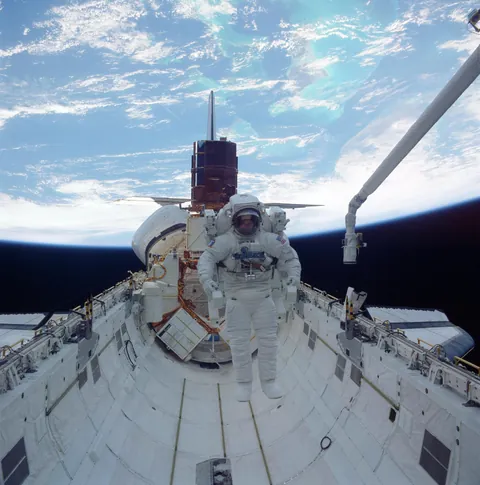 Astronaut James van Hoften wearing the Manned Maneuvering Unit while traversing Challenger's payload bay during STS-41-C.