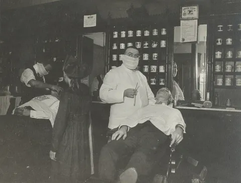 2 barbers use masks while working due the Spanish flue crisis, circa 1918