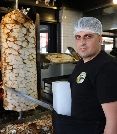 Turkish döner kebab master straps ice to his waist to survive the heat next to the vertical meat furnace.